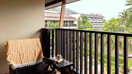 Parveke, jossa tuoli, pöytä ja näkymä kasvillisuuteen ja rakennuksiin. (Tekoälyn luoma teksti)