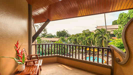 Kuva parvekkeesta, jossa on puinen pöytä ja tuoli, näkymä puutarhaan ja uima-altaalle. (Tekoälyn luoma teksti)