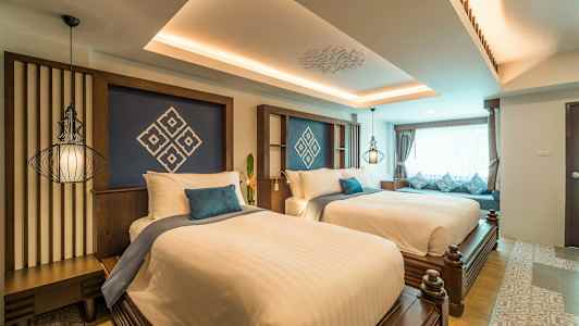 Hotellihuone, jossa on kaksi leveää sänkyä, koristeltu valkoisilla lakanoilla ja sinisillä tyynyillä, sekä suuri ikkuna, jossa on verhot. (Tekoälyn luoma teksti)