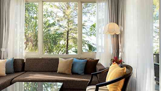 Olohuone, jossa sohva ja tyynyjä ikkunoiden edessä, näkyy vihreyttä. (Tekoälyn luoma teksti)