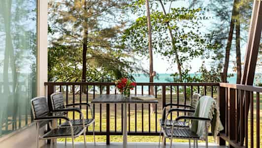 Näkymä verannalta, jossa on pöytä ja tuolit, taustalla meri ja puita. (Tekoälyn luoma teksti)