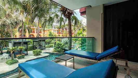 Näkymä parvekkeelta, jossa kaksi sinistä aurinkotuolia, ja edessä värikäs puutarha palmujen ja uima-altaan kanssa. (Tekoälyn luoma teksti)