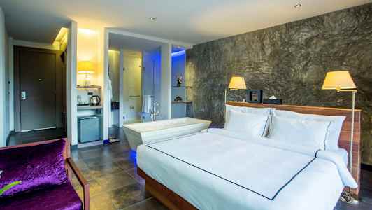 Moderni hotellihuone, jossa on parisänky, kylpyamme vieressä ja tyylikäs sisustus. (Tekoälyn luoma teksti)