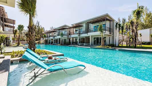 Kuva aurinkotuoleista uima-altaan äärellä nykyaikaisten lomahuoneistojen edessä. (Tekoälyn luoma teksti)