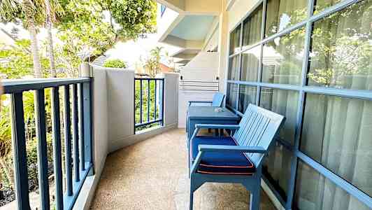 Parvekkeen kuva, jossa on kaksi sinistä tuolia, pöytä ja näkymä puiden ja vihreyden suuntaan. (Tekoälyn luoma teksti)