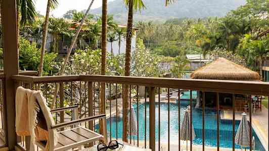 Näkymä parvekkeelta altaalle, jota ympäröivät palmut ja vehreät kasvit, etualalla tuoli ja pöytä. (Tekoälyn luoma teksti)