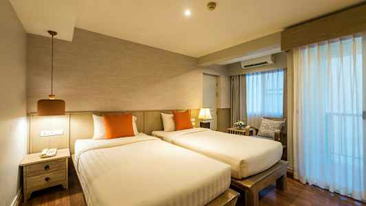 Kaksi sänkyä oransseilla tyynyillä huoneessa, jossa on puuyksityiskohtia ja valoa läpäiseviä verhoja. (Tekoälyn luoma teksti)