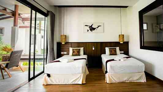 Kahden hengen huone, jossa on kaksi yhden hengen vuodetta, ikkuna ja koristetyynyt. (Tekoälyn luoma teksti)