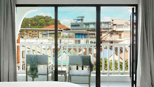 Näkymä suuren lasi-ikkunan läpi parvekkeelle, jolta avautuu kaupunkimaisema. (Tekoälyn luoma teksti)