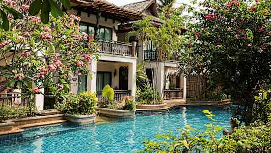 Uima-allas, jossa on sininen vesi, ympäröitynä trooppisilla kasveilla ja parvekkeellisella rakennuksella. (Tekoälyn luoma teksti)