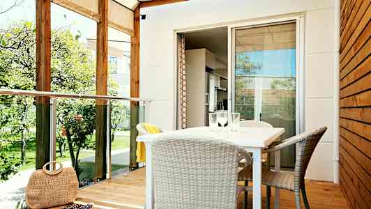 Veranda, jossa on katto, pöytä ja tuolit sekä näkymä puutarhaan. (Tekoälyn luoma teksti)