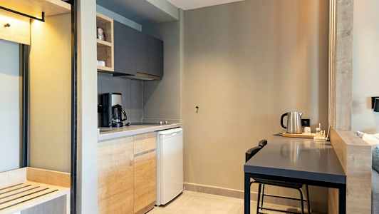 Keittiö, jossa puukaapit, kahvinkeitin, jääkaappi ja pöytä vedenkeittimellä. (Tekoälyn luoma teksti)