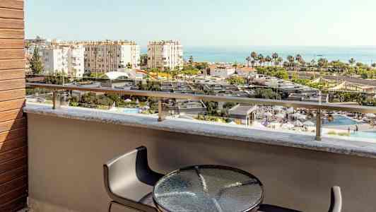 Näkymä parvekkeelta, jossa on pöytä ja tuolit, yli uima-altaan ja rakennusten kohti merta. (Tekoälyn luoma teksti)