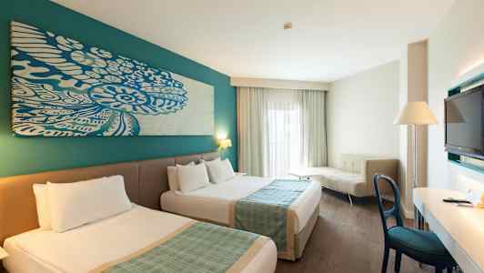 Hotellihuone, jossa kaksi sänkyä, kirjoituspöytä, sohva ja televisio. (Tekoälyn luoma teksti)