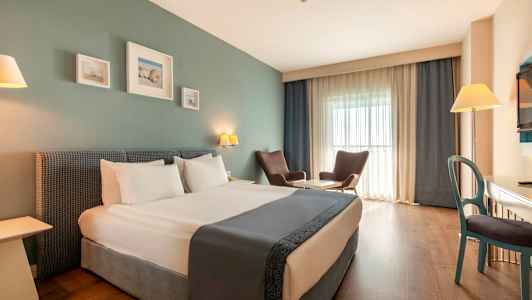 Hotellihuone, jossa on parivuode, kaksi nojatuolia pöydän ääressä, kirjoituspöytä ja televisio. (Tekoälyn luoma teksti)