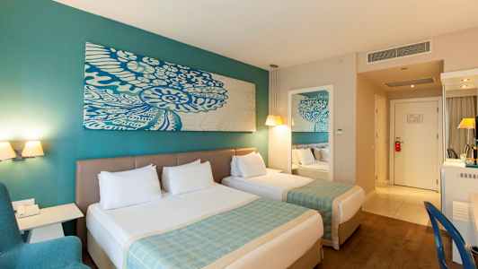 Kaksi sänkyä valkoisilla vuodevaatteilla hotellihuoneessa, turkooseilla yksityiskohdilla ja modernilla sisustuksella. (Tekoälyn luoma teksti)