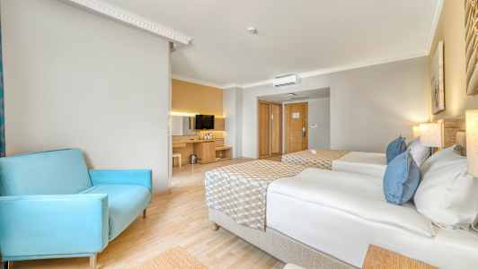 Hotellihuone, jossa kaksi yhden hengen vuodetta, sininen tuoli ja televisio lipaston päällä. (Tekoälyn luoma teksti)