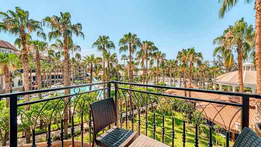 Näkymä parvekkeelta puutarhaan, jossa on palmupuita ja rakennuksia taustalla. (Tekoälyn luoma teksti)