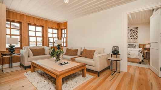 Olohuone, jossa sohvia ja sohvapöytä, puupaneeliseinät ja ikkunat sekä avaus makuuhuoneeseen. (Tekoälyn luoma teksti)