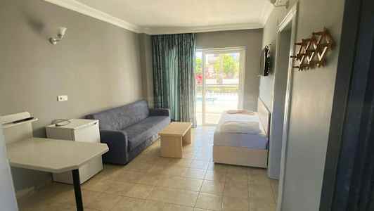 Hotellihuone, jossa on sohva, pöytä ja sänky, sekä näkymä parvekkeelle. (Tekoälyn luoma teksti)