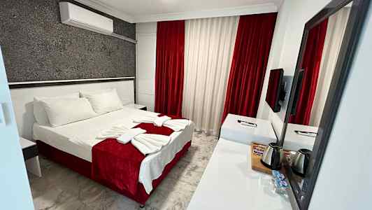 Hotellihuone, jossa on parivuode, valkoista ja punaista sisustusta sekä kirjoituspöytä ja peili. (Tekoälyn luoma teksti)