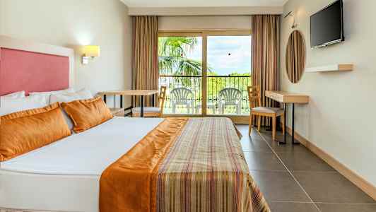 Hotellihuoneen sisätila, jossa on iso sänky, parveke ulkokalusteilla ja televisio seinällä. (Tekoälyn luoma teksti)