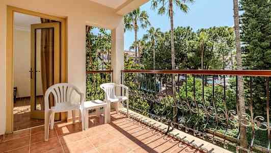 Parveke, jossa ovi, kaksi valkoista muovituolia ja näkymä puihin ja kasvillisuuteen. (Tekoälyn luoma teksti)