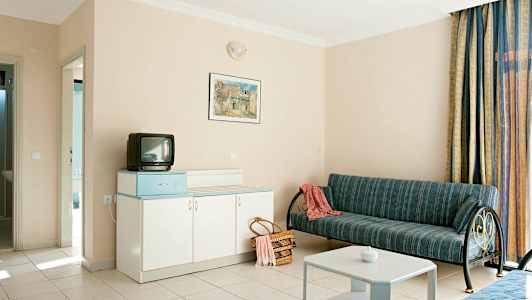 Hotellihuone, jossa sohva, pöytä, kaappi ja pieni televisio. (Tekoälyn luoma teksti)