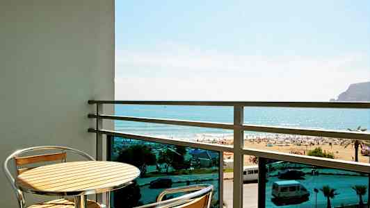 Parveke, jossa pöytä ja kaksi tuolia, näkymä rannalle ja merelle. (Tekoälyn luoma teksti)