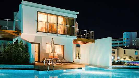 Valkoinen rakennus uima-altaan edessä, kuvattu illalla. (Tekoälyn luoma teksti)