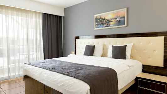 Moderni hotellihuone, jossa kaksoisvuode, harmaa päiväpeite ja seinällä oleva taulu. (Tekoälyn luoma teksti)