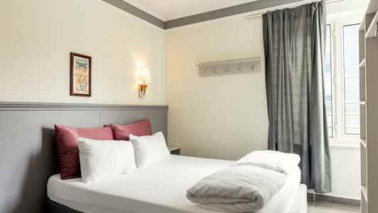 Kuva hotellihuoneesta, jossa on parivuode, koristeltu valkoisilla ja punaisilla vuodevaatteilla sekä vaaleanharmaa sängynpääty. (Tekoälyn luoma teksti)