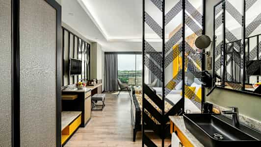 Kuva modernista hotellihuoneesta, jossa on työpöytä, tuoli ja televisio sekä erillinen makuutila. (Tekoälyn luoma teksti)