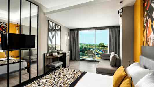 Moderni hotellihuone, jossa sänky, sohva ja näkymä parvekkeelle panoraamanäkymällä. (Tekoälyn luoma teksti)