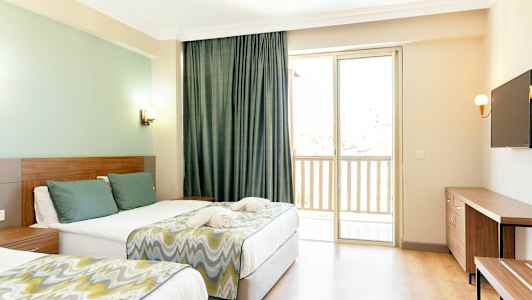 Hotellihuone, jossa on kaksi sänkyä, seinällä televisio ja ikkuna parvekkeelle. (Tekoälyn luoma teksti)