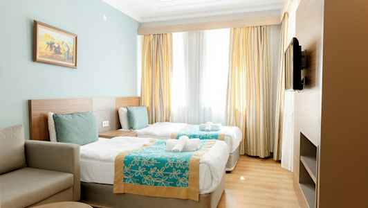 Hotellihuone, jossa kaksi erillisvuodetta, sohva ja seinällä televisio. (Tekoälyn luoma teksti)