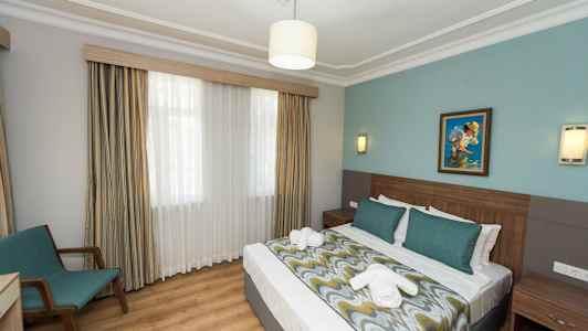 Hotellihuone, jossa on parivuode, sängynvalaisimet, maalaus seinällä ja tuoli ikkunan ääressä. (Tekoälyn luoma teksti)