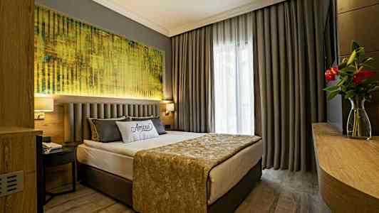 Hotellihuone, jossa parisänky, harmaat verhot ja taulu sängyn yläpuolella. (Tekoälyn luoma teksti)