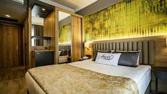 Moderni hotellihuone, jossa on parivuode, koristeellinen tyyny ja värikäs seinätaide. (Tekoälyn luoma teksti)