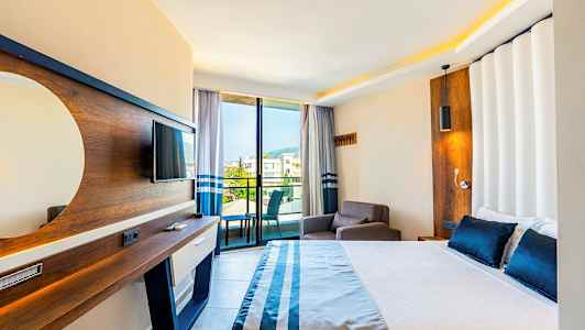 Hotellihuone, jossa sänky, nojatuoli, televisio ja parveke näkymällä. (Tekoälyn luoma teksti)