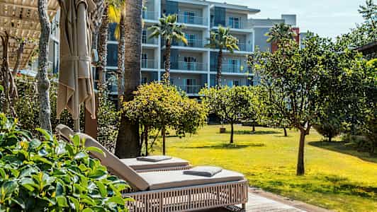 Kaksi aurinkotuolia terassilla, josta on näköala nurmikolle ja puihin, taustalla huoneistohotelli. (Tekoälyn luoma teksti)