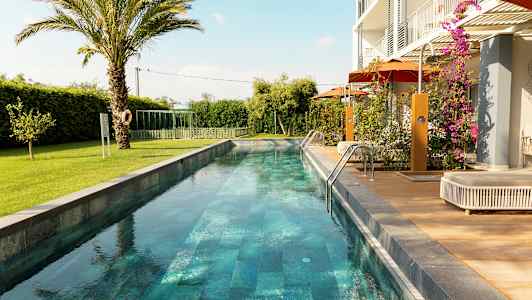 Pitkä ja kapea uima-allas ympäröitynä viheralueilla ja modernilla asumisella. (Tekoälyn luoma teksti)