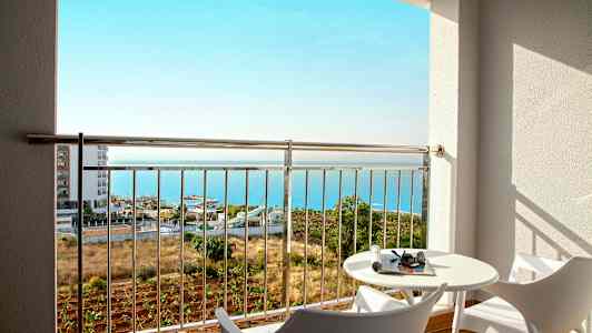 Näkymä parvekkeelta, jossa on kaksi modernia tuolia, pöytä ja meri taustalla. (Tekoälyn luoma teksti)