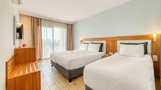 Moderni hotellihuone, jossa on kaksi sänkyä, vaaleat värit ja suuret ikkunat. (Tekoälyn luoma teksti)