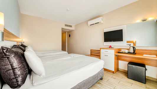 Hotellihuone, jossa on kaksi sänkyä, työpöytä, peili ja seinään kiinnitetty TV. (Tekoälyn luoma teksti)