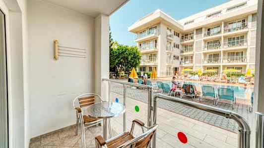 Parveke, jossa on pöytä ja tuolit, avautuu uima-altaalle ja hotellille. (Tekoälyn luoma teksti)