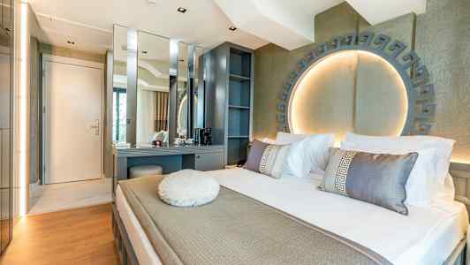 Moderni hotellihuone, jossa sänky, työpöytä ja koristeellinen valaistus. (Tekoälyn luoma teksti)