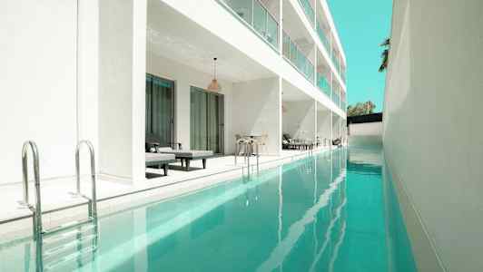 Kuva pitkästä uima-altaasta modernin valkoisen rakennuksen vieressä, jossa on yksityisiä istumapaikkoja. (Tekoälyn luoma teksti)