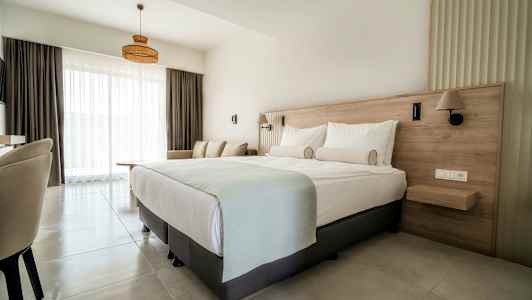 Hotellihuone, jossa on parivuode, sohva ja suuret ikkunat vaaleilla verhoilla. (Tekoälyn luoma teksti)