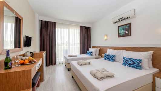 Hotellihuone, jossa on kaksi yhden hengen sänkyä valkoisilla lakanoilla ja sinisillä tyynyillä sekä pöytä, jossa on hedelmiä ja juomia. (Tekoälyn luoma teksti)